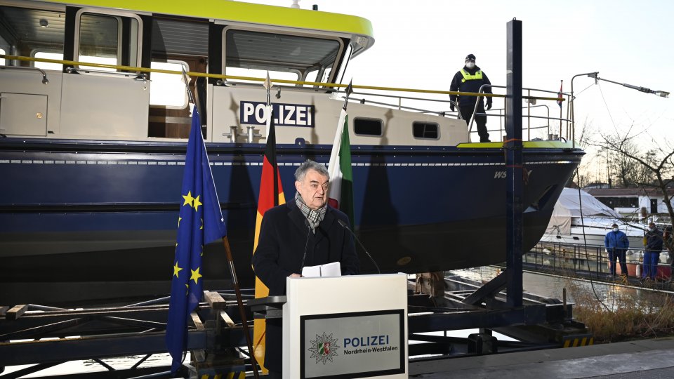 Minister Herbert Reul am Stehpult vor der Europa- Deutschland und Landesfahne vor dem Boot der Wasserschutzpolizei