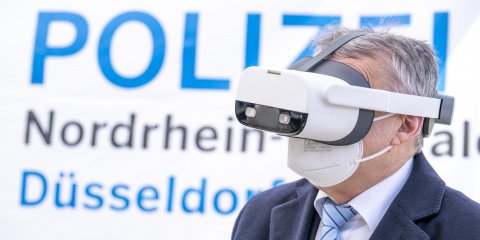 Innenminister Herber Reul mit einer Virtual-Reality-Brille vor einem Plakat der Polizei NRW