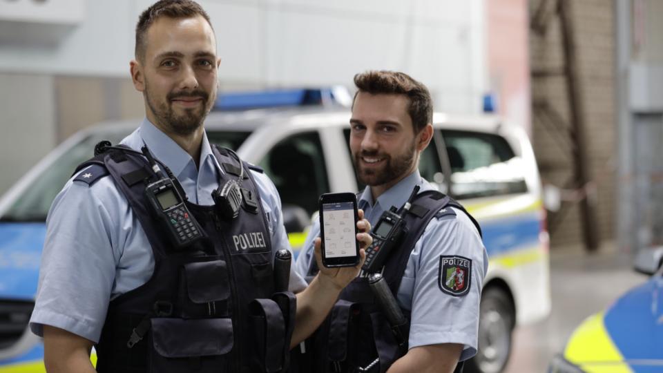 Start Auslieferung Handys für Polizei NRW-  Zwei Polizisten vor Streifenwagen mit Handy