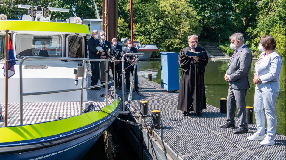 Ein Geistlicher bei der Bootstaufe vor dem Boot mit weiteren Gästen