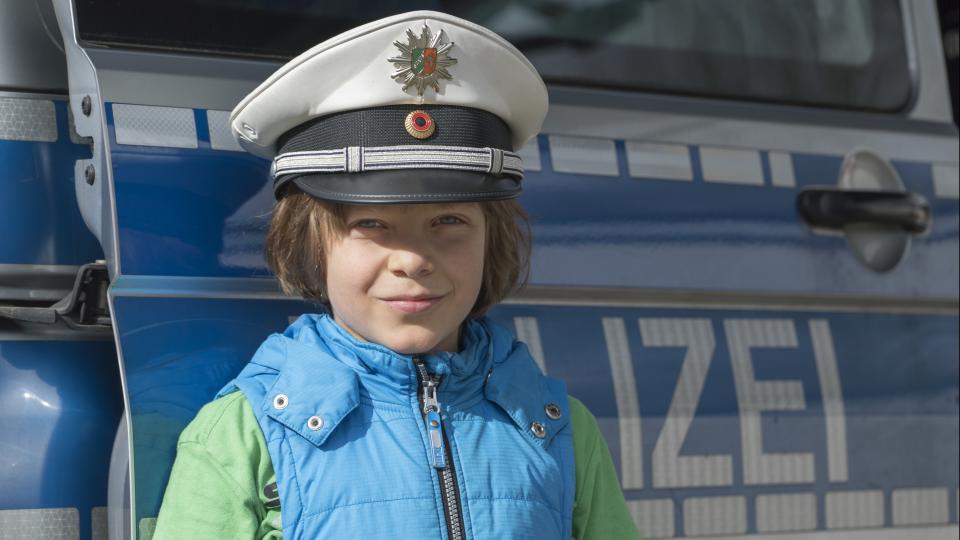 Kind mit Polizeimütze vor Polizeiauto