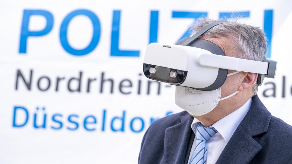 Innenminister Herber Reul mit einer Virtual-Reality-Brille vor einem Plakat der Polizei NRW