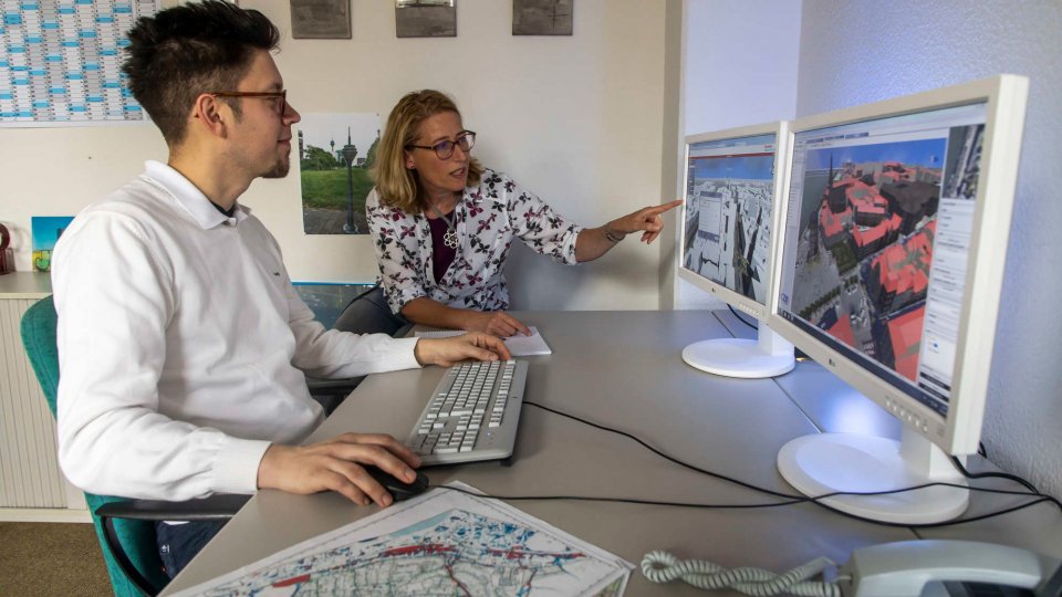 Geomatiker an Arbeitsplatz mit Karten auf Bildschirmen