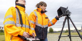 Zwei Frauen stehen draußen auf einem Platz und vermessen etwas.