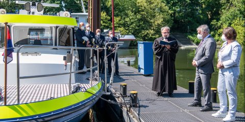 Ein Geistlicher bei der Bootstaufe vor dem Boot mit weiteren Gästen