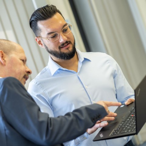 Zwei Herren schauen gemeinsam auf einen Laptop und diskutieren